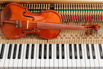 classic brown violin on the close up image of grand piano keys and interior showing strings, hammer...