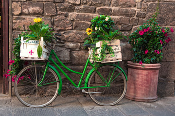 Fototapeta na wymiar Beautiful city landscape with a green bike near the old wall with flowers in drawers in Florence, Italy, Europe.