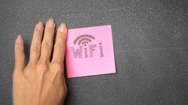 Closeup woman's hand sticking note with Wifi word on the blackboard - video in slow motion