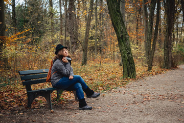 Naklejka na ściany i meble Woman sitting on a bench in a park on a autumn day
