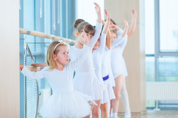 Young ballerinas rehearsing in the ballet class. They perform different choreographic exercises. They stand in different positions near the ballet barr.