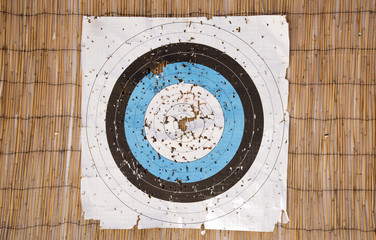 A paper archery target face with many holes torn into the target area