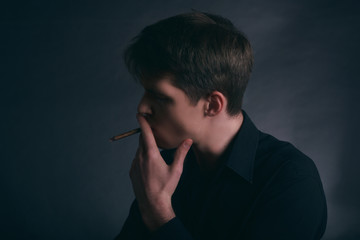 Man is smoking a cigar. Boy smoking cigarette on the dark background.