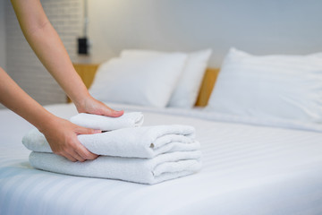 Close-up of hands putting stack of fresh white bath towels on the bed sheet. Room service maid...