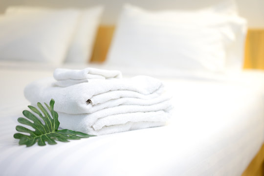 Stack of White hotel towel with green leafs on bed decoration in bedroom interior.