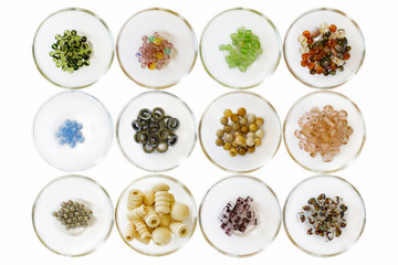 Different types of beads; isolated on white in small glass bowls; wooden; meta; glass; sparkle; stone; and opaque beads displayed in glass bowls