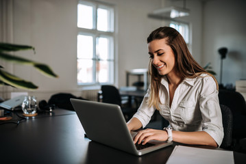 Smiling brunette girl working on a laptop at modern office