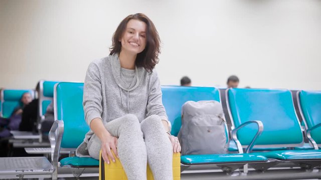 Cheerful and happy young woman is sitting on her luggage and laughing.
