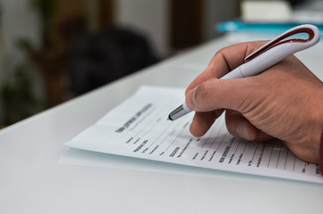 Closeup on hand of a person signing document contract form on light table background