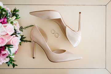Wedding bouquet of the bride of pink flowers roses and greens, stylish elegant classic lacquered beige shoes and two silver wedding rings lying on pastel background. Close up. flat lay. top view.