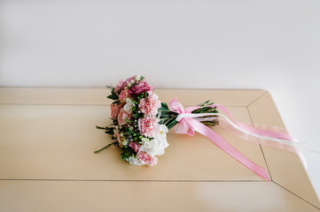 Stylish wedding bouquet bride of pink roses, white carnation and green flowers and greens with ribbons lying on pastel table. Close up. Side view. Wedding decor. Artwork.