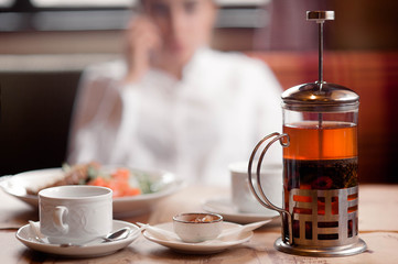 On the table in the cafe there is a Cup of fruit tea, jam and a kettle with tea
