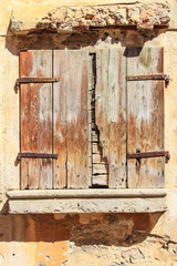 Altes Fenster mit verwitterten geschlossenen Holzläden in gelber abgebröckelter Fassade