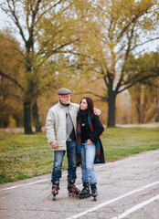 A happy pensioner laughs and stands on roller skates on the road and hugs his daughter in an autumn park.