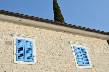 Two windows with blue wooden jalousies on a coastal house facade