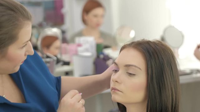 Portrait of young beautiful woman and stylist in make up salon tweezes eyebrow