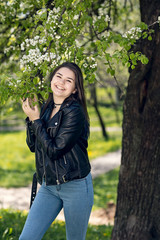 Glamorous young caucasian woman in black leather jacket in a flowery garden