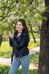 Glamorous young caucasian woman in black leather jacket in a flowery garden