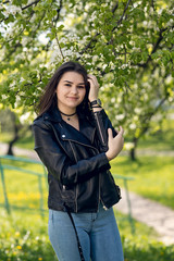 Glamorous young caucasian woman in black leather jacket in a flowery garden