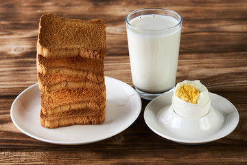 Breakfast with egg, toasts and glass of fresh milk on a rustic wooden table background, close-up. Healthy vegetarian breakfast and diet concept. Levitation food concept