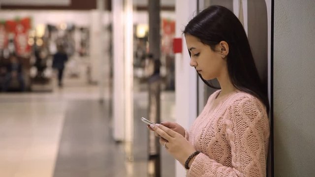 Profile of ah elegant young woman touching the screen of her smartphone and seeking some business information while standing in a shopping mall