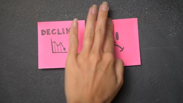 Closeup woman's hand sticking note with sad face icon next to the Decline word on the blackboard - video in slow motion