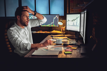 Young male trader at office work concept sitting looking at computer disappointed