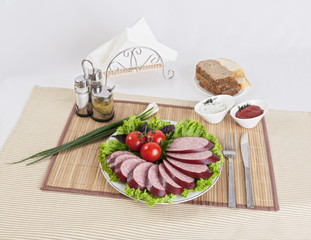Smoked sausage with tomatoes and lettuce leaves on a plate.