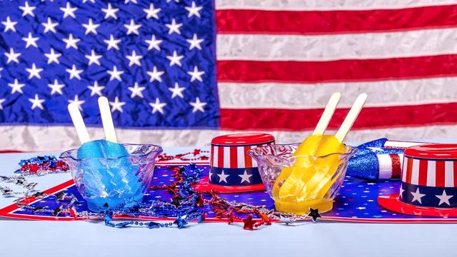 Two popsicles in clear cups melting against a colorful American patriotic backdrop celebrating July fourth and Memorial Day.