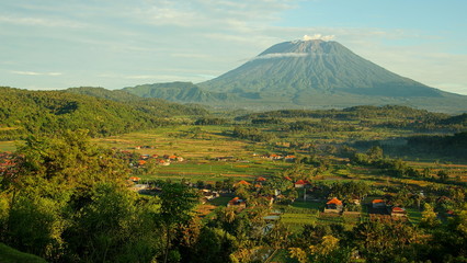 malerischer Vulkan Mt.Agung  hinter grünen Reisfeldern und vereinzelten Häusern