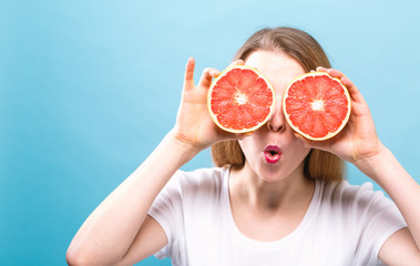 Happy young woman holding grapefruits on a blue background