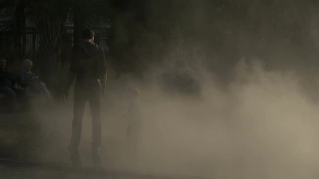 A man and a boy walking through artificial smoke