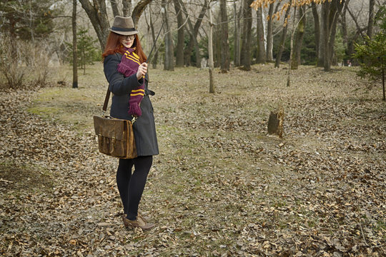 A witch girl with a magic wand in her hand, wearing glasses, a coat, a hat and a scarf, with a vintage bag, pronounces a spell