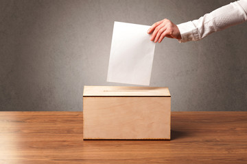 Ballot box with person casting vote on blank voting slip, grungy background