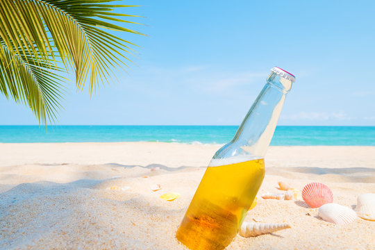 Beer bottle on a sandy beach with palm tree. vintage color tone effect