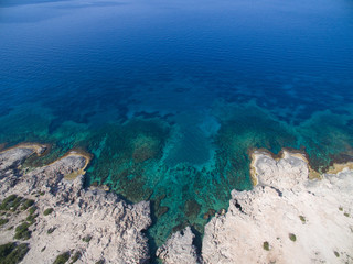 Aerial view of rock formations, cliffs and transparent waters sea shore with beach