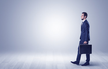 Successful businessman walking in front of an empty wall with briefcase on his hand
