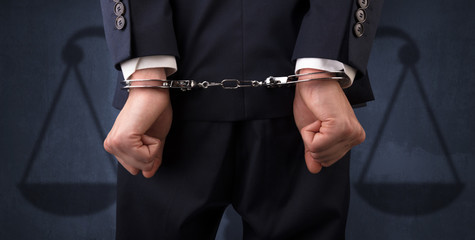 Arrested businessman in handcuffs with hands behind back and justice symbol wallpaper
