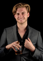 Male model in a classy dark suit isolated against a black background. Model holding whiskey