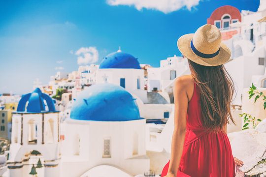 Fototapeta Tourist traveling in Santorini, Oia island in Greece, Europe travel summer vacation woman relaxing at view of three blue domes church famous attraction. holiday girl in hat and red dress enjoying sun.