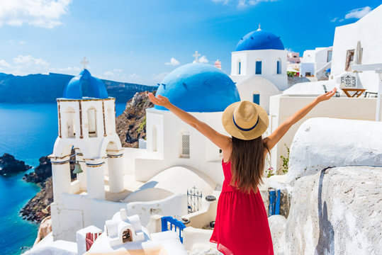 Fototapeta Europa podróży szczęśliwa kobieta wakacje. Dziewczyna turysta ma zabawę z otwartymi rękami w wolności w Santorini rejsu wakacje, lato europejczyka miejsce przeznaczenia. Czerwona sukienka i kapelusz osoba.