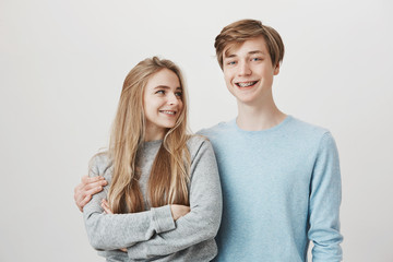 Girlfriend knows boyfriend prepared something for anniversary. Portrait of two friendly caring siblings, hugging and smiling broadly, wearing shiny braces. Girl looking at guy who dare to cuddle her