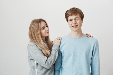 Sister trying to comfort brother who lost in competition. Portrait of caring worried blond cute woman hugging and looking with care and sympathy at man who frowns and feeling upset, being in bad mood
