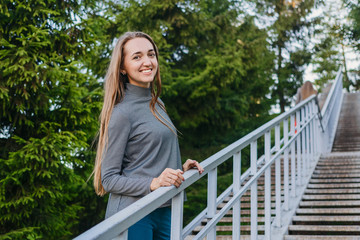 beautiful slender woman in grey pullover with long hair, standing on the stairs in summer Park