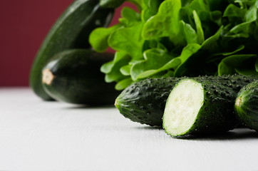 Green vegetables - salad spinach, cut cucumbers, zucchini on  white wood board, closeup. Healthy vegeterian raw summer food ingredients.