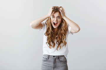 Stop yelling at me, cannot handle pressure. Indoor shot of fed up intense blonde in glasses, pulling hair and shouting, outraged and depressed, arguing or relieving stress over gray background