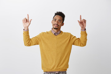 Naklejka premium What a disappointment. Portrait of displeased doubtful american guy with afro hairstyle raising hands and pointing up with index fingers, expressing disgust and doubt, standing over gray background