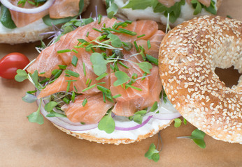 Bagel sandwich with creame cheese, salmon,onion,tomato,greens,chives close-up on a wooden background. Delicious bagel, golden bake color, soft inside, crispy outside.