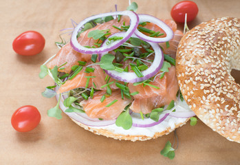 Bagel sandwich with creame cheese, salmon,onion,tomato,greens,chives close-up on a wooden background. Delicious bagel, golden bake color, soft inside, crispy outside.
