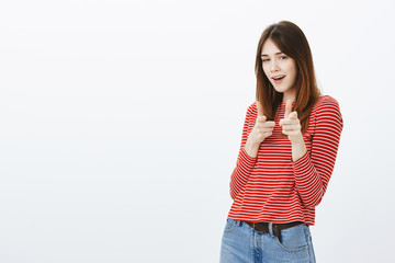 Checking you out. Portrait of playful beautiful girl in casual outfit, showing finger gun gesture and pointing joyfully at camera, having interesting idea in ming or greeting best friend